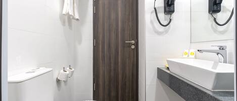 Un baño moderno con puerta de madera oscura, azulejos blancos, un lavabo blanco con encimera de granito y dos secadores de pelo fijos en la pared.