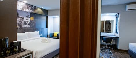 A hotel room with a bed, bedside table with coffee makers, a desk with a chair, and a mirror.