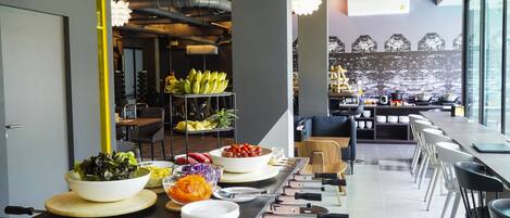 Une cuisine moderne dotée d’un long comptoir, de divers aliments et offrant une vue sur le paysage urbain grâce à de grandes fenêtres.