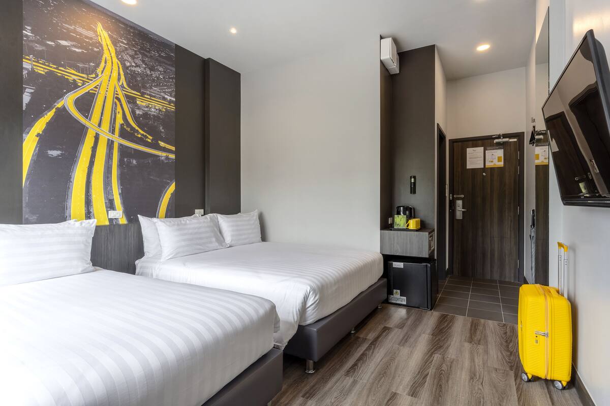 A hotel room with two beds, a large abstract painting, a small kitchenette, and a suitcase.