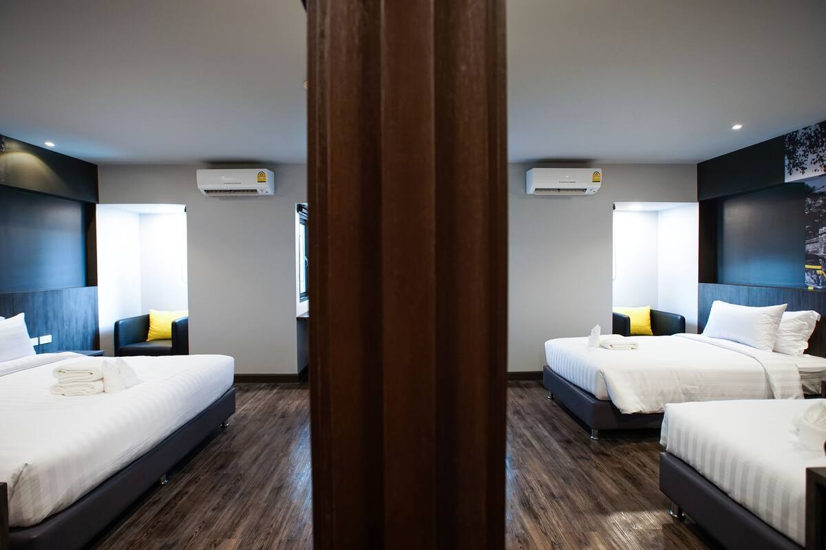 A hotel room with two beds, dark wood flooring, white bedding, and air conditioning units on the walls.