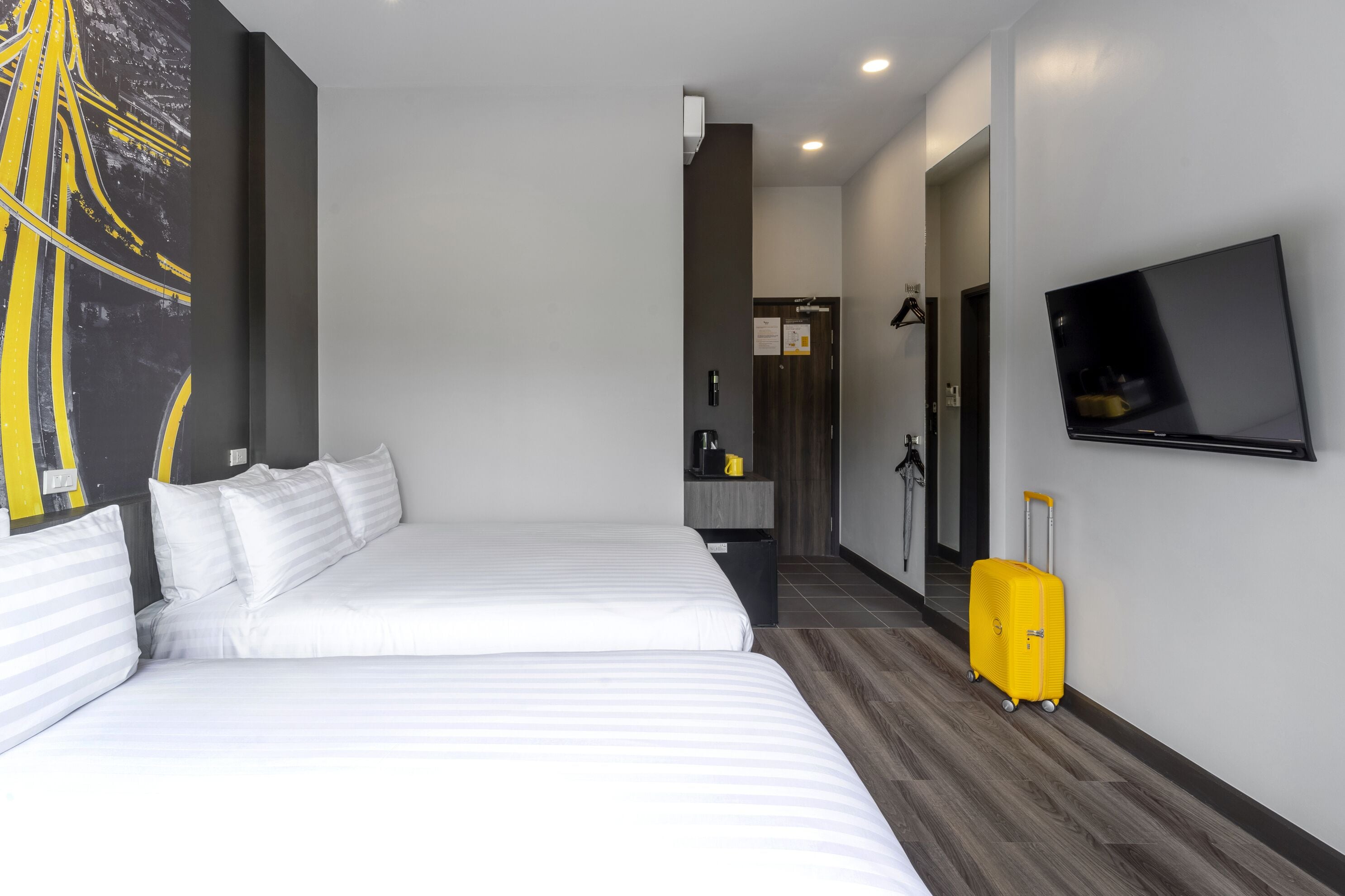 Habitación de hotel con dos camas, un televisor, una maleta amarilla y un cuadro en la pared.