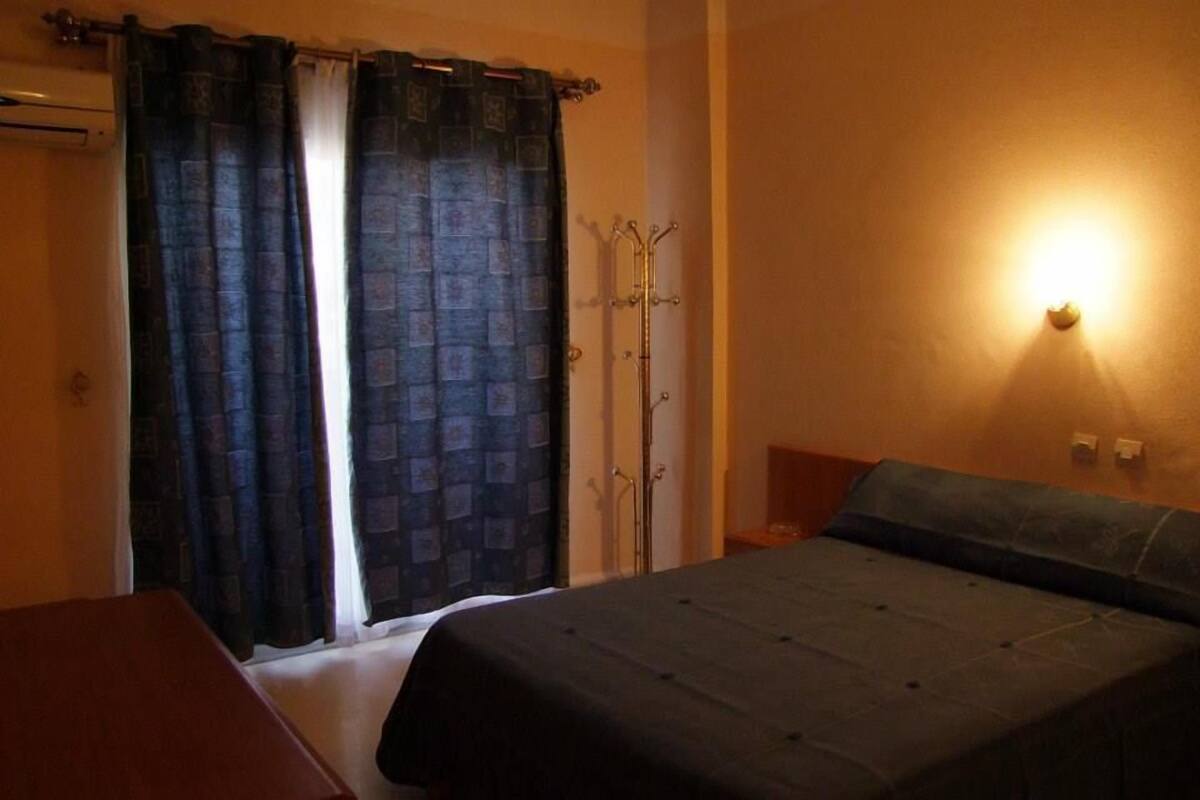A bedroom with a bed, a nightstand, a wardrobe, and a wall-mounted light fixture.