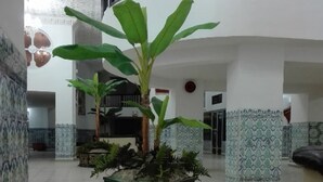 Een ruime lobby met een patroon van tegels, een centrale plantenbak met een grote plant, en een gebogen plafond.