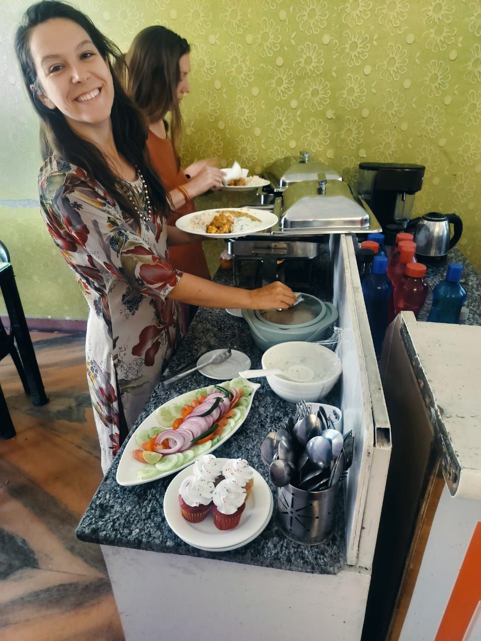 A buffet setup with various dishes, including a plate of cupcakes and a salad, and a coffee machine.