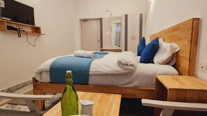A neatly made bed with a wooden headboard, a bedside table, and a small wooden shelf above the bed. - Chakrah by Hermitage (Narendranagar)