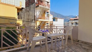 A balcony with a table and two chairs, overlooking a residential area with buildings and mountains in the background. - Chakrah by Hermitage (Narendranagar)