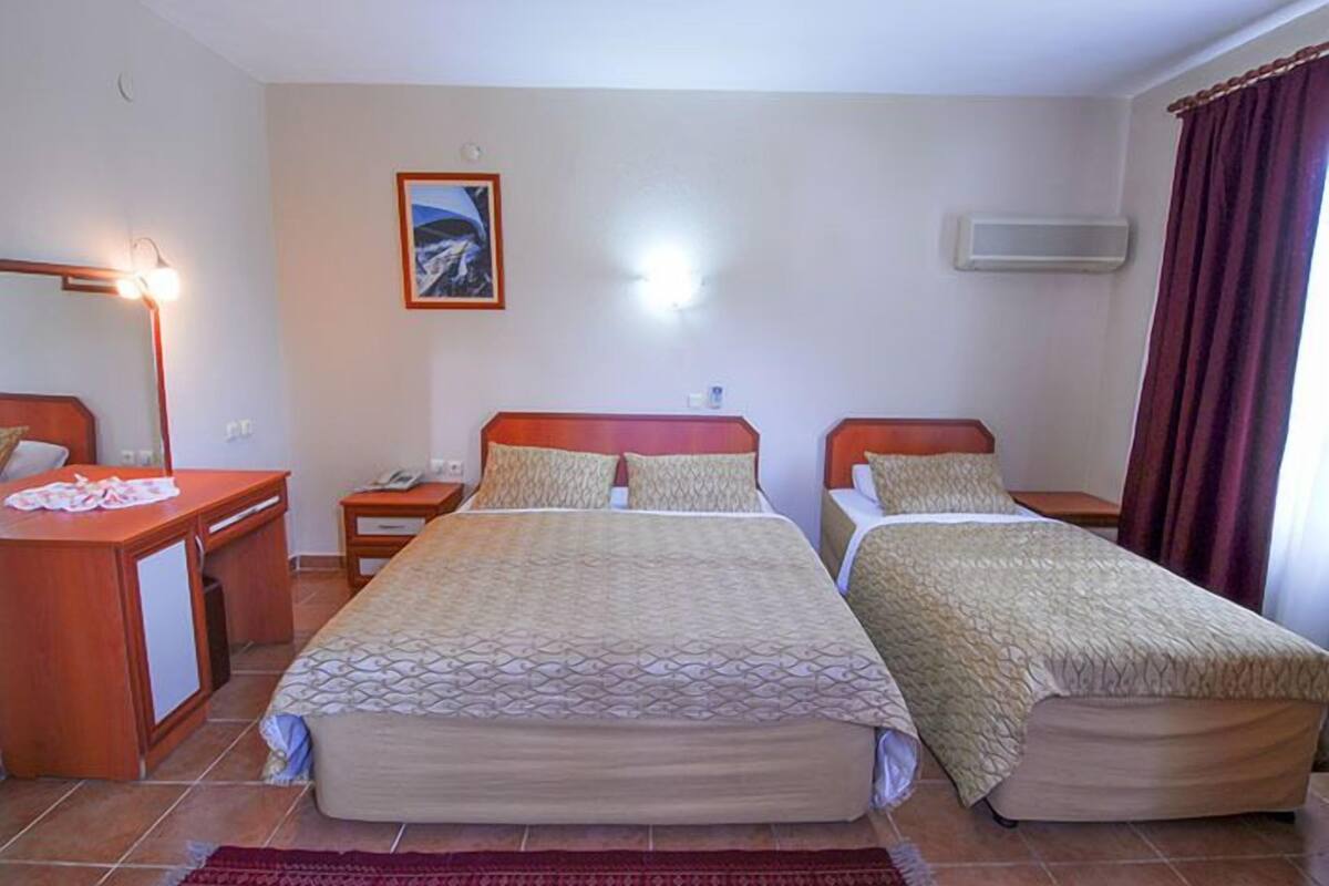 A hotel room with two beds, a desk, a chair, a lamp, a picture on the wall, and an air conditioning unit.