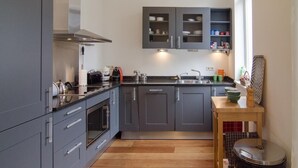 Una cocina moderna con armarios grises, una campana extractora de acero inoxidable y una mesa de madera con un bol y una tetera.