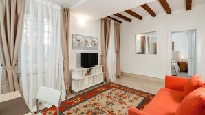 Ein Wohnzimmer mit einem Fernseher auf einem weißen Schrank, einem gemusterten Teppich und einem orangefarbenen Sofa.