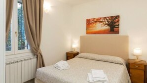 Ein Hotelzimmer mit Bett, Nachttisch mit Lampe, Vorhängen am Fenster und einem Gemälde an der Wand.