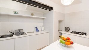 Eine moderne Küche mit weißen Schränken, einer Edelstahlspüle, einem Gasherd und einer Obstschale auf der Arbeitsfläche.