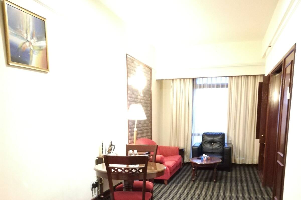 A hotel room with a bed, a desk, a chair, a sofa, a lamp, and a view of the outside through a window.