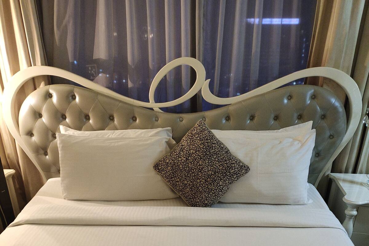 A neatly made bed with a tufted headboard, a patterned pillow, and a plain white pillow.