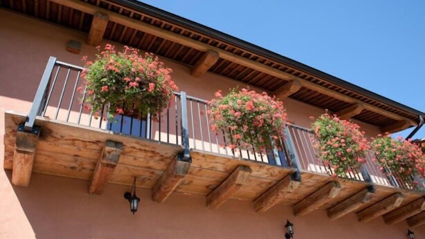 A building with wooden balconies, each with a railing and potted plants. - Il Torchio Snc (Pianfei)