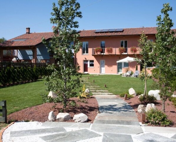 A two-story house with a stone pathway leading to the front door, surrounded by a well-maintained lawn and a few trees. - Il Torchio Snc (Pianfei)