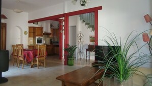 A dining area with a wooden table and chairs, a kitchen in the background, and a staircase leading to another level. - Charming town on 400m² of fully enclosed land (Elne)