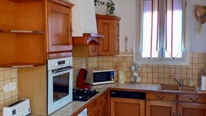 A compact kitchen with wooden cabinets, a microwave, a toaster, and a dishwasher. - Charming town on 400m² of fully enclosed land (Elne)