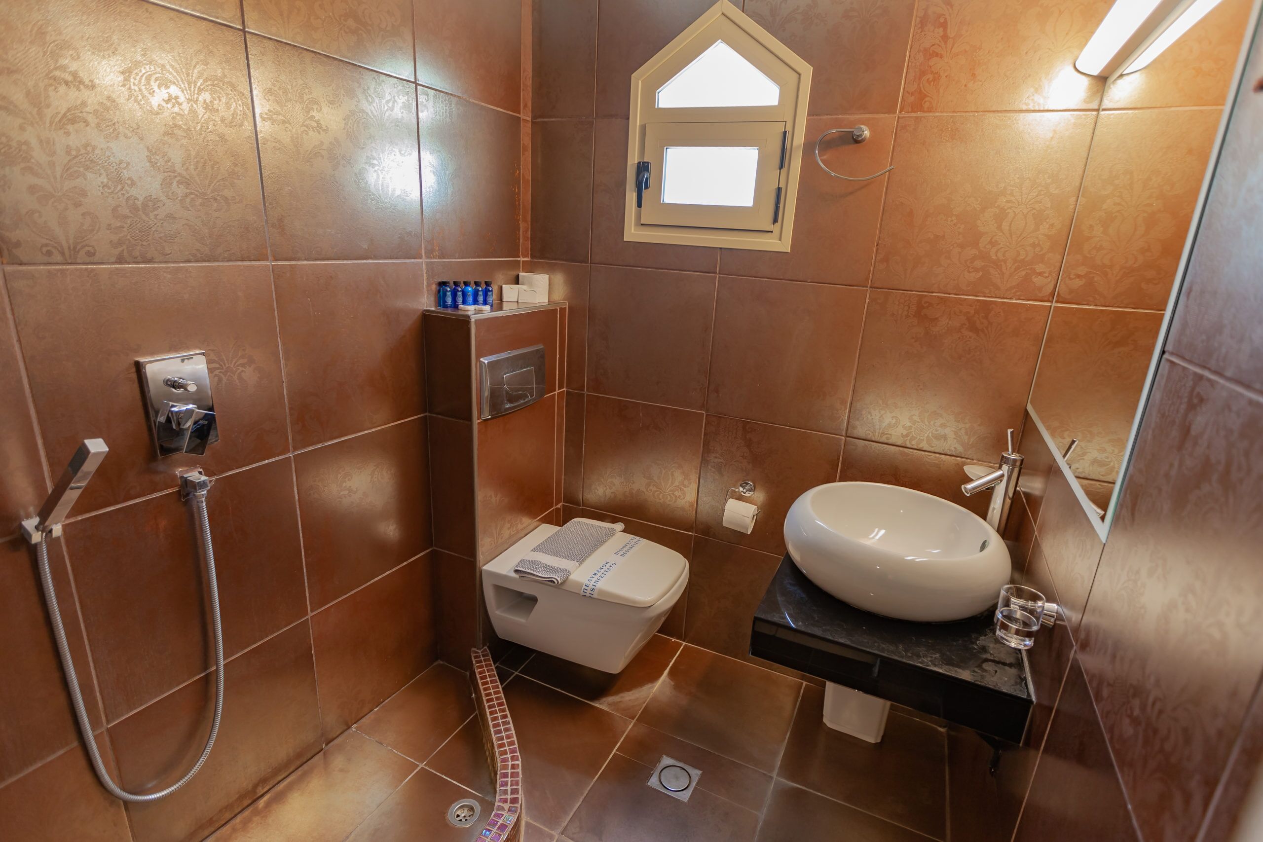 A bathroom with a toilet, sink, shower, and a small window.