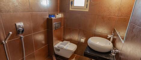 A bathroom with a toilet, sink, shower, and a small window.