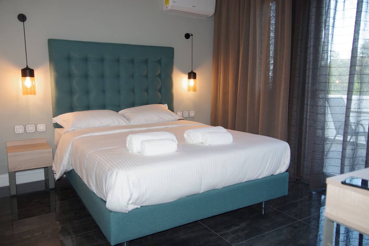 A neatly made bed with white linens and two rolled towels, a teal upholstered headboard, and two bedside lamps.
