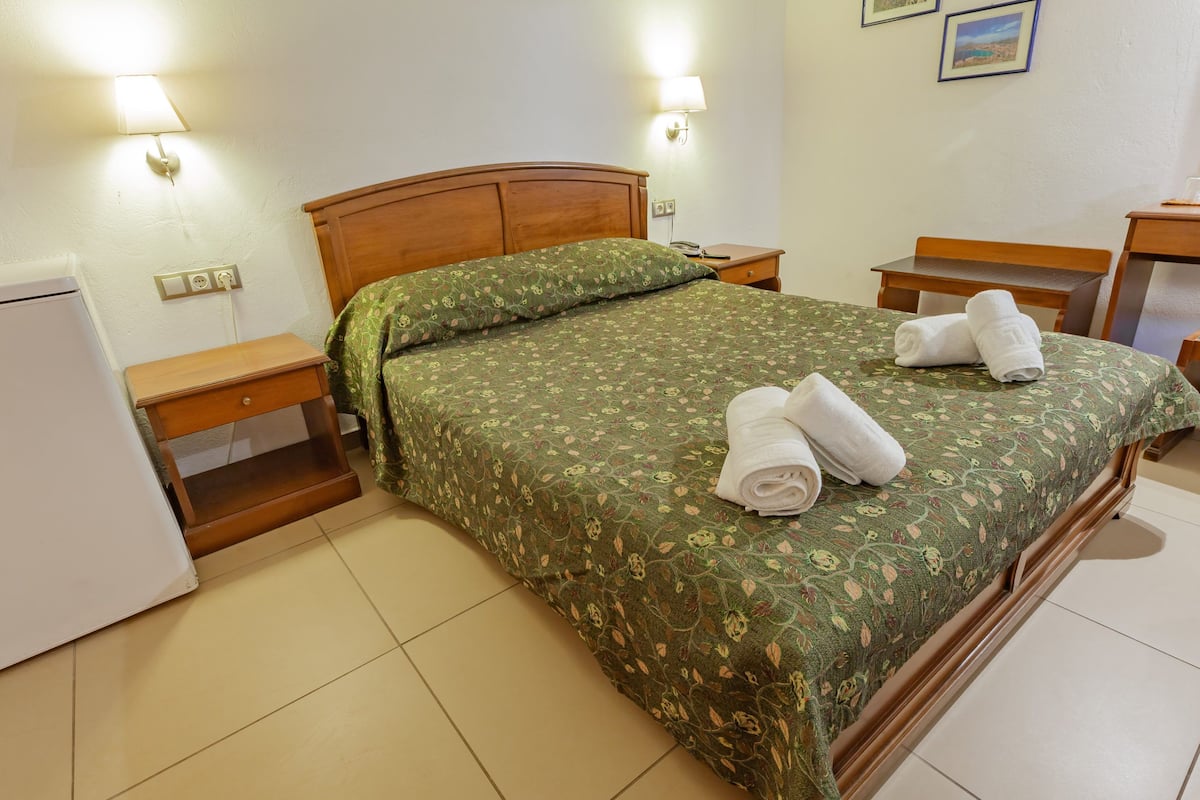 A neatly made bed with floral bedding, two bedside lamps, a wooden nightstand, and a small table with a chair.