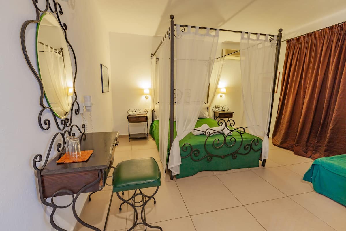 A bedroom with a four-poster bed, a bedside table with a lamp, a green chair, and a large mirror on the wall.