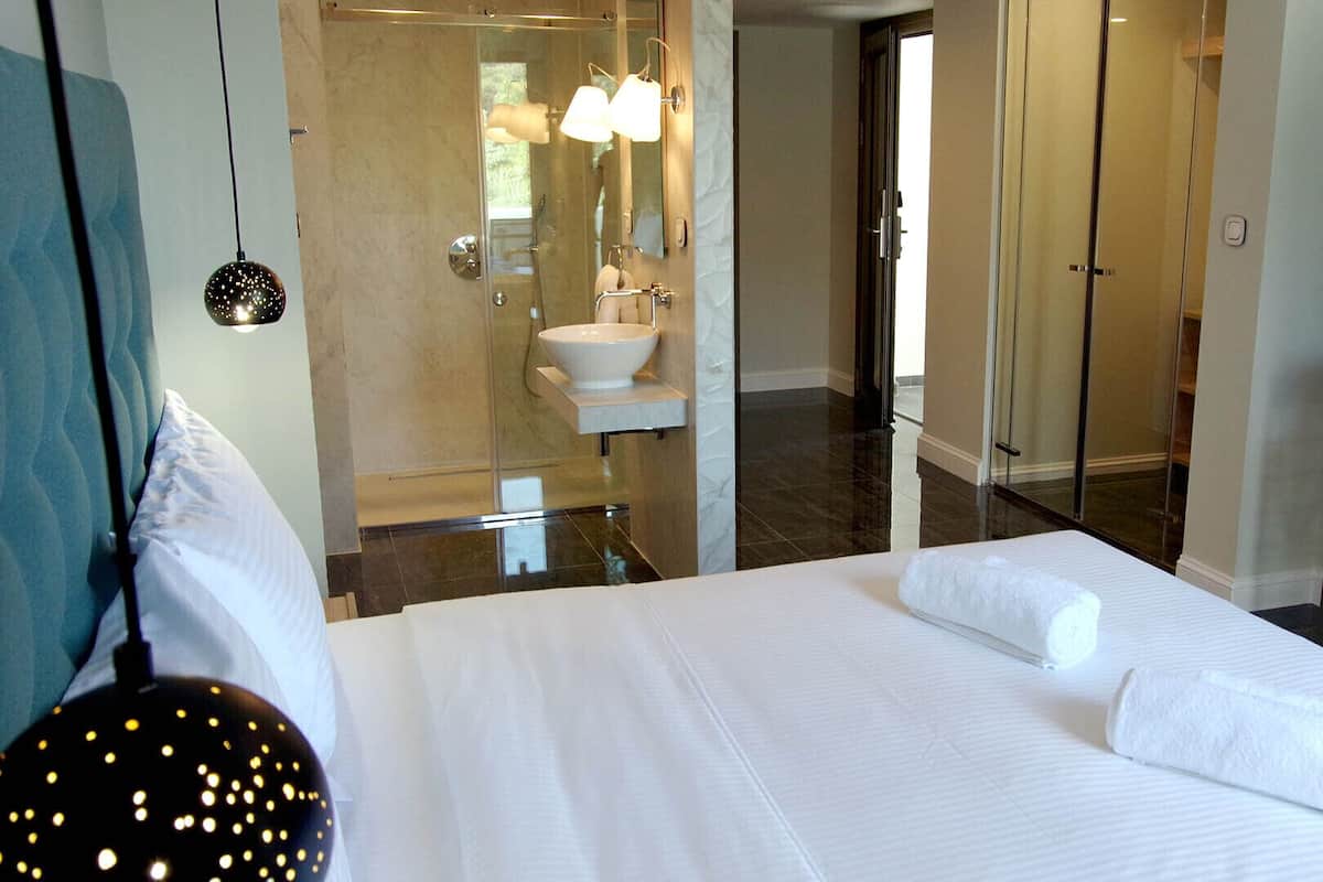 A hotel room with a large bed, a bathroom with a sink and mirror, and a coffee machine on a side table.