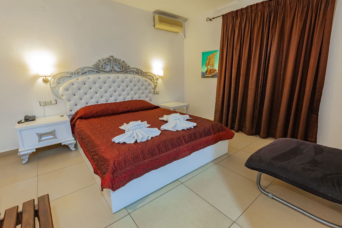 A neatly arranged bedroom with a large bed, a bedside table with a lamp, a small bedside table with a phone, and a bench.