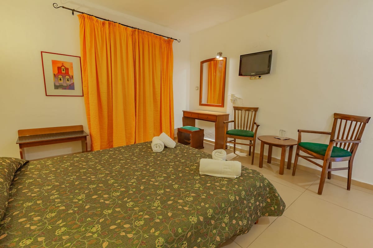 A hotel room with a bed, a desk, two chairs, a TV, and a painting on the wall.