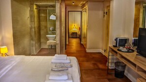 Habitació d'hotel amb un llit, un bany, una televisió i una taula amb una safata de gots i una tassa.