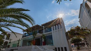 Edifici modern amb façana de vidre, escala que condueix a l'entrada i cel blau amb el sol radiant.