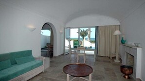 Uma sala de estar ampla com sofá, mesa de centro e lareira. Há uma varanda com vista para o mar.