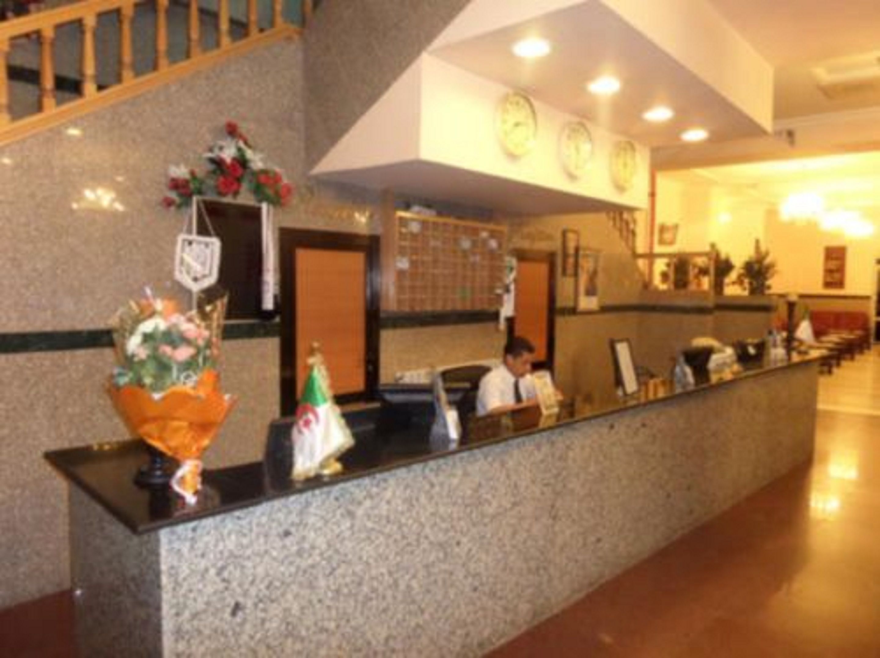 Zona de recepción de hotel con mostrador de mármol, un reloj y un mostrador de atención al cliente.