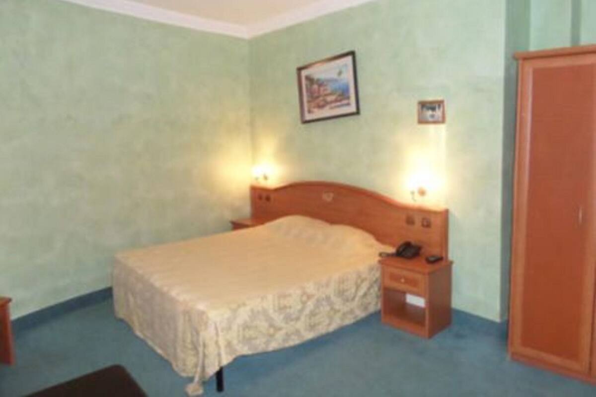 A bedroom with a bed, bedside tables, a nightstand, a wardrobe, and a painting on the wall.