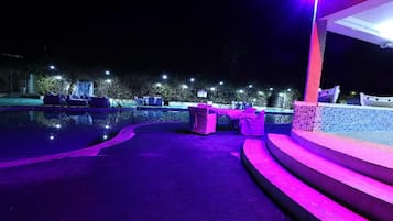 A nighttime pool area with seating and steps leading to a covered area.