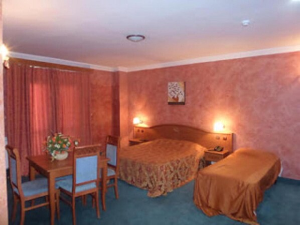 Quarto de hotel com cama, mesas de cabeceira, escrivaninha com cadeira e uma pequena mesa com um vaso de flores.