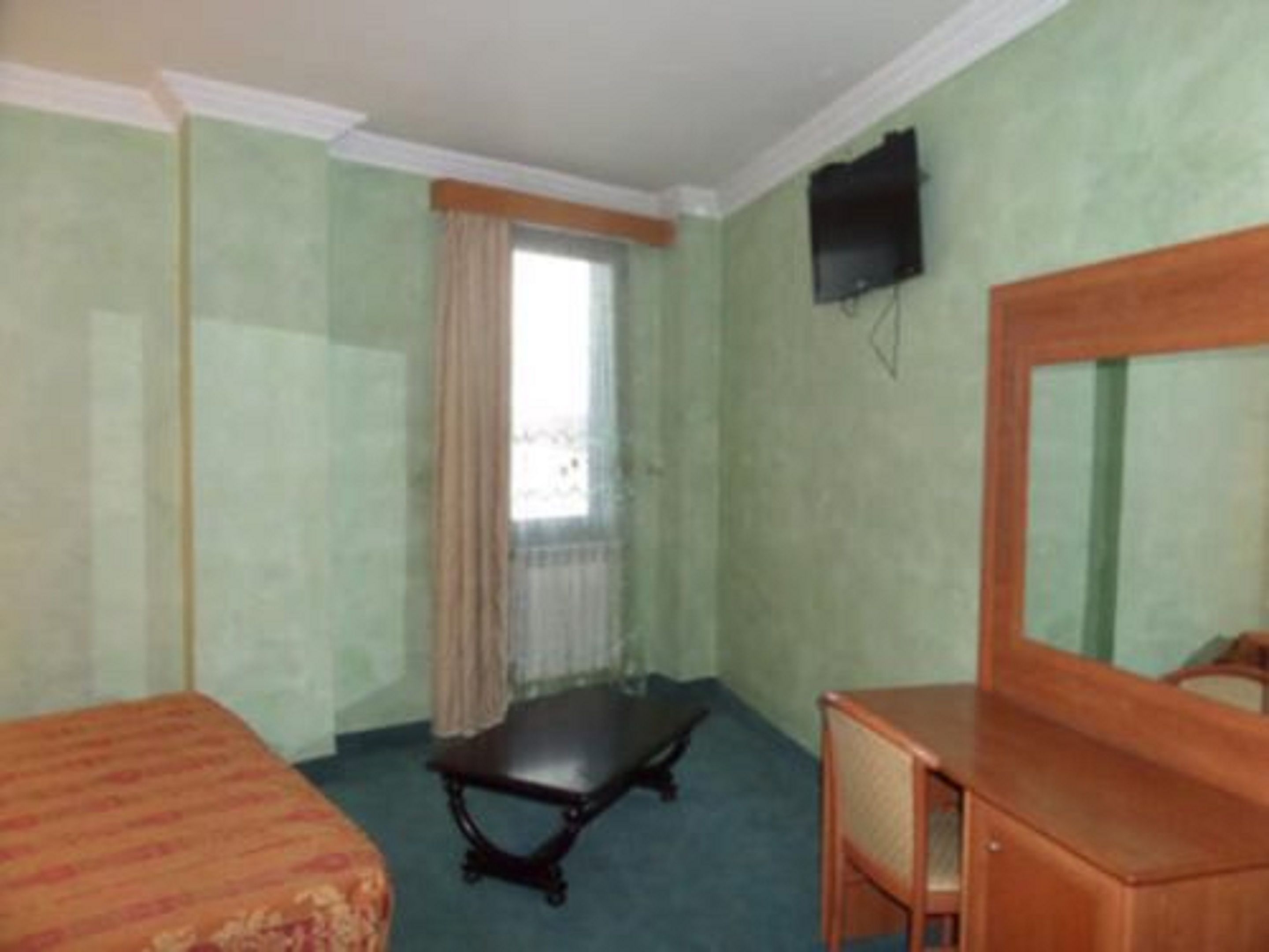 Una habitación con cama, escritorio, silla, televisión y ventana con cortinas.
