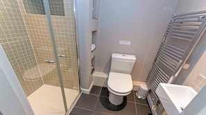A bathroom with a glass shower enclosure, a toilet, and a towel rack.