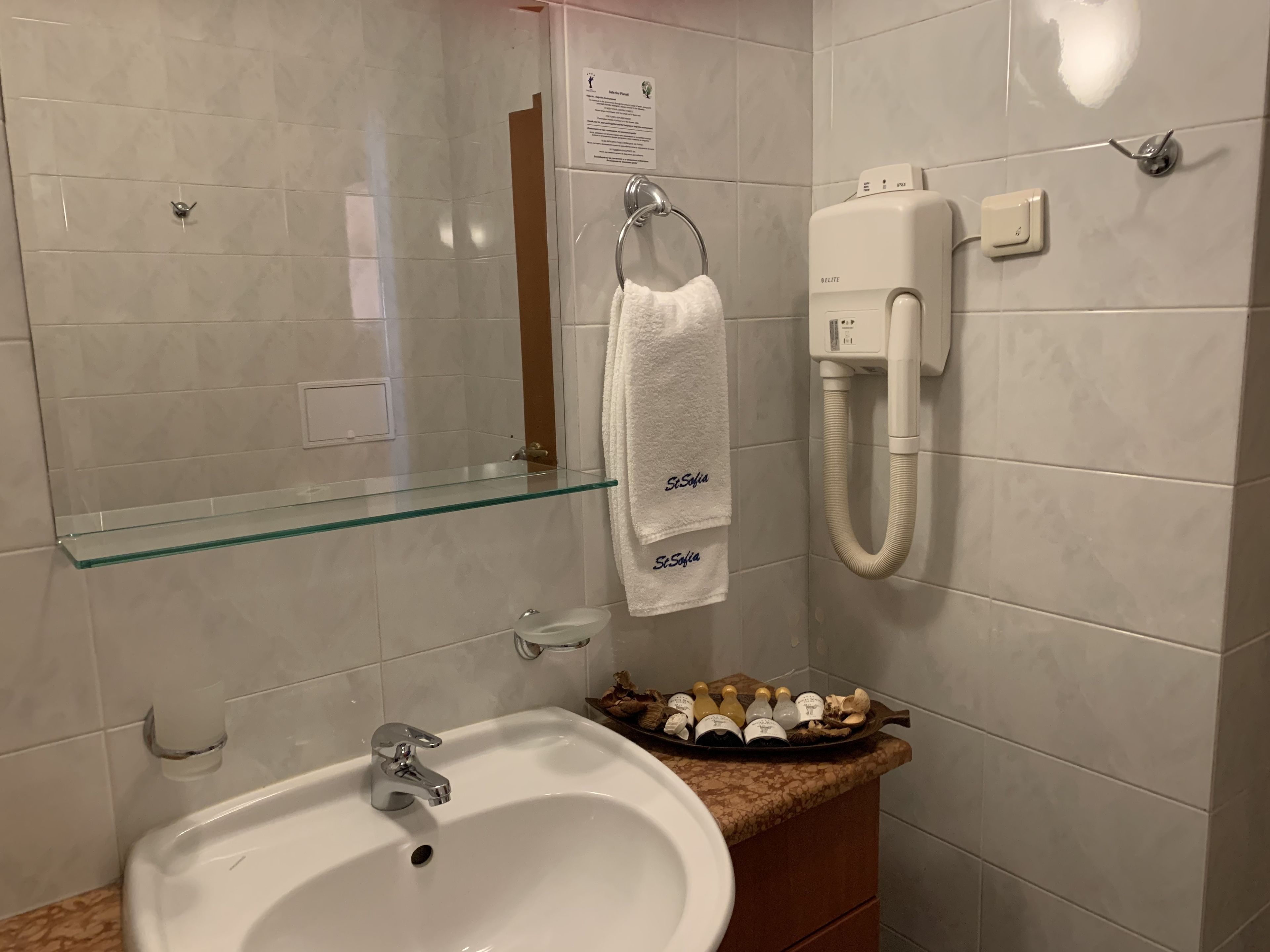 Un baño con repisa de vidrio, lavamanos, toallero y teléfono.