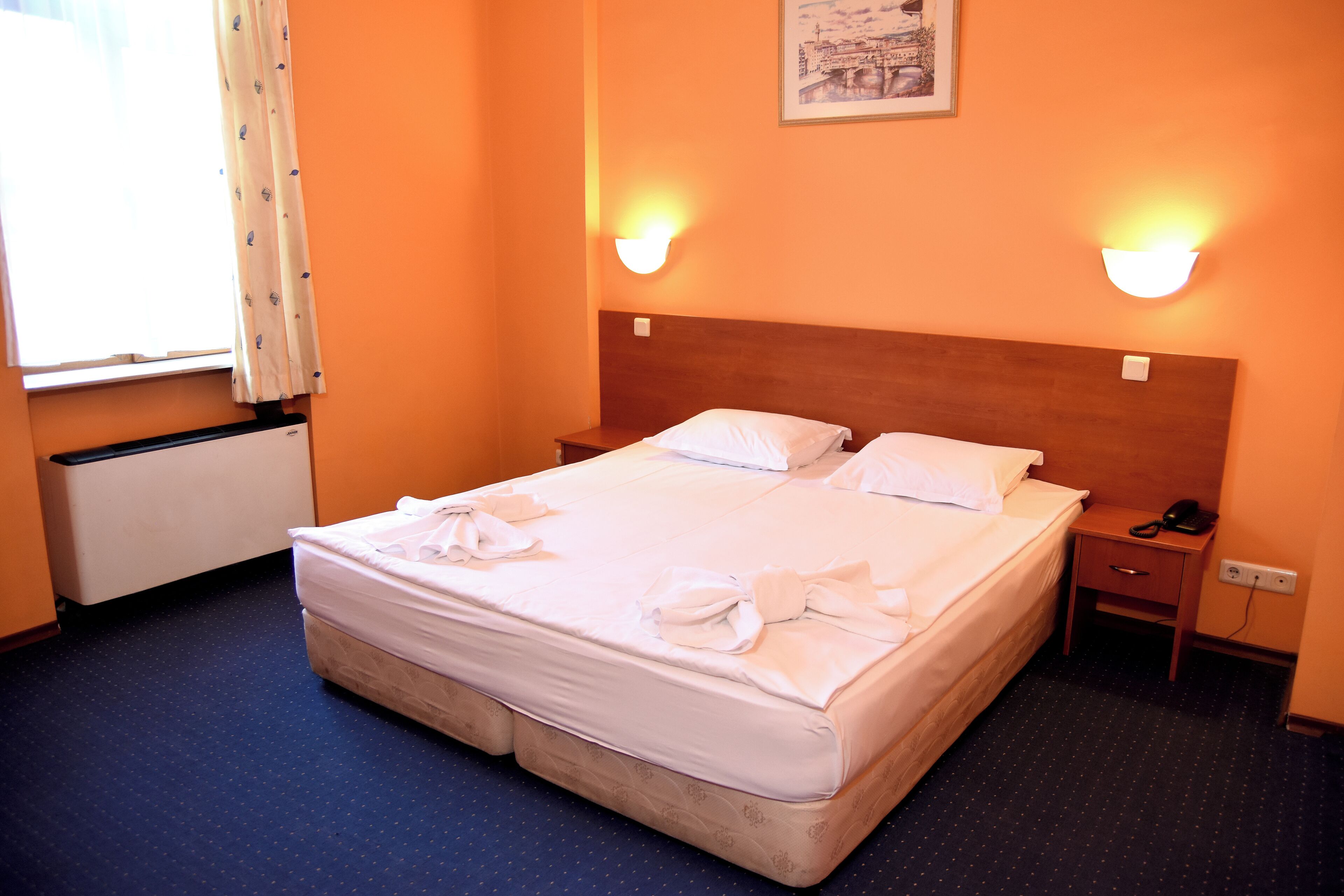 A hotel room with a bed, bedside tables, a nightstand, and a window with curtains.