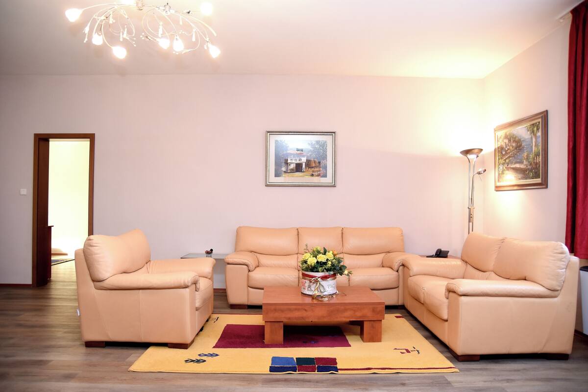 Una sala de estar con un sofá color beige, una mesa de centro de madera con un centro de mesa floral y un cuadro en la pared.