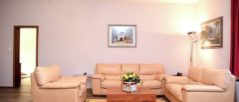 A living room with a beige sofa set, a wooden coffee table with a floral centerpiece, and a framed picture on the wall.
