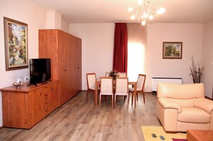 Una sala de estar con un mueble de madera, una televisión, una mesa de comedor con sillas, un sofá y dos cuadros en las paredes.
