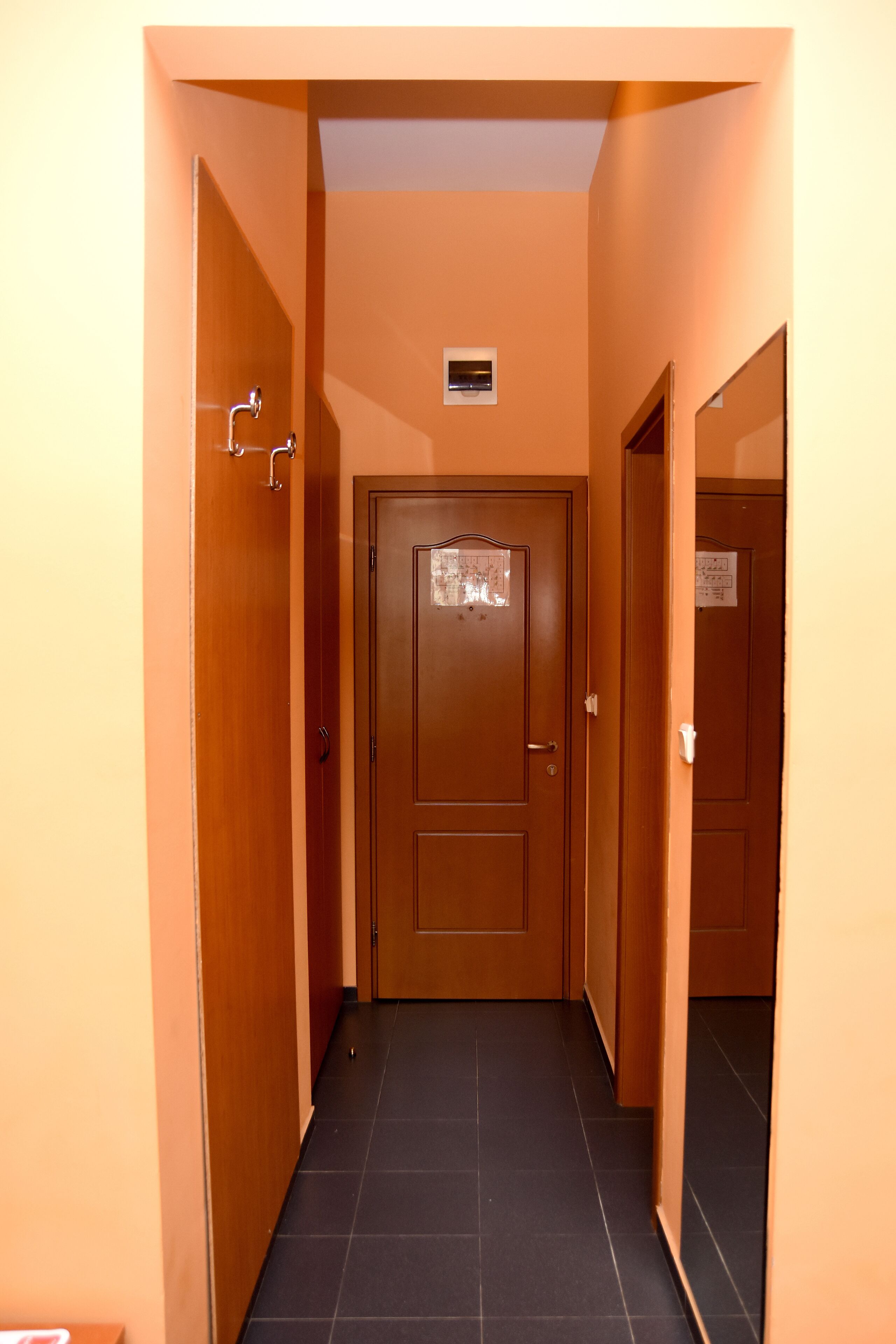 Un pasillo estrecho con puertas de madera y suelo de baldosas negras.