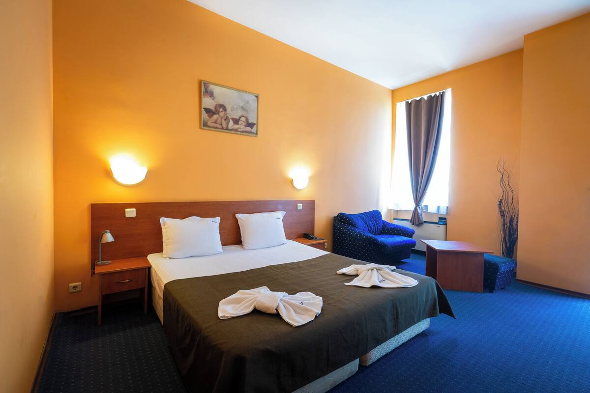 Habitación de hotel con una cama grande, dos mesitas de noche, un escritorio, una silla y una ventana con cortinas.