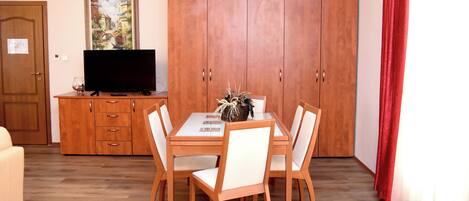 Un comedor con una mesa de madera, sillas blancas, un televisor sobre un mueble de madera y un amplio armario.