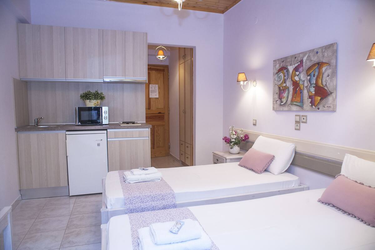 A compact hotel room with a kitchenette, two beds, a painting, and a small bathroom.