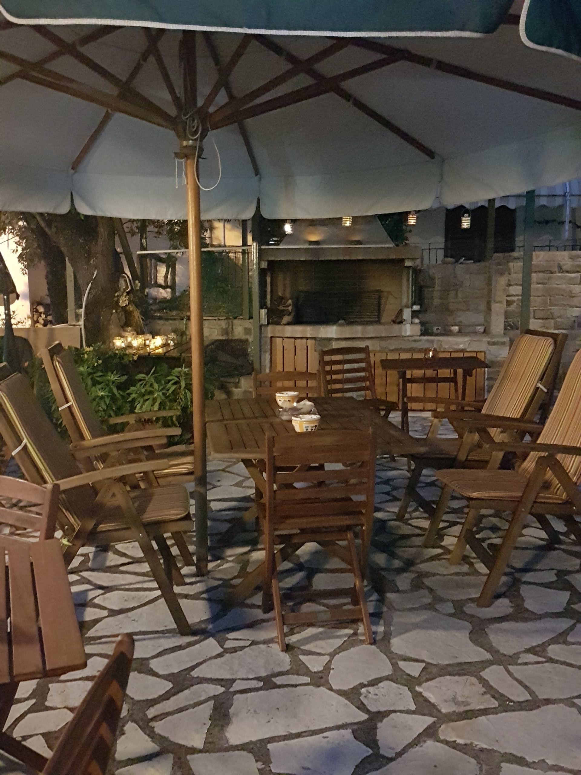 Ulkoterassi, jossa on kivilaattalattia, puiset huonekalut ja suuri aurinkovarjo.