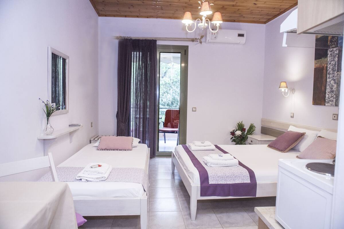 A hotel room with two beds, a bathroom, a wooden ceiling, and a view through a door.